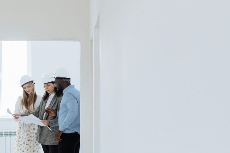 Team mit Bauhelmen prüft Baupläne im Rohbau, Baustellenbesichtigung und Projektbesprechung im Innenraum.