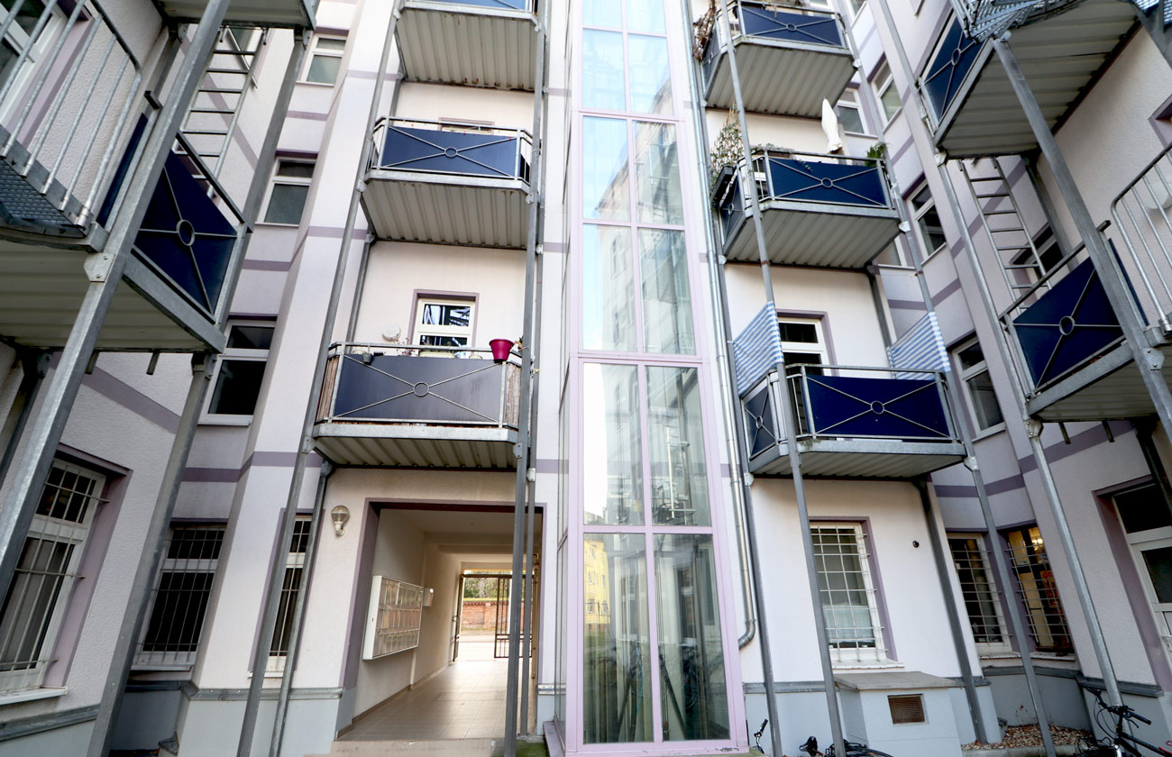 Moderner Innenhof mit verglastem Aufzug, Balkonen und &uuml;berdachtem Durchgang in Mehrfamilienhaus.