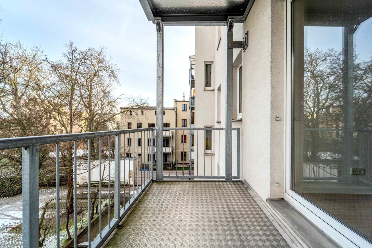 Balkon mit Metallgel&auml;nder und Blick in begr&uuml;nten Innenhof einer modernen Wohnanlage, urbanes Wohnen mit Au&szlig;enbereich.