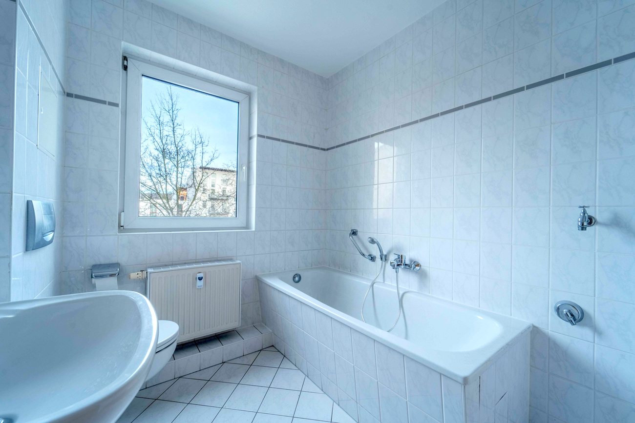 Helles gefliestes Bad mit Badewanne, WC, Waschbecken und Fenster, funktionale Ausstattung in moderner Wohnung.