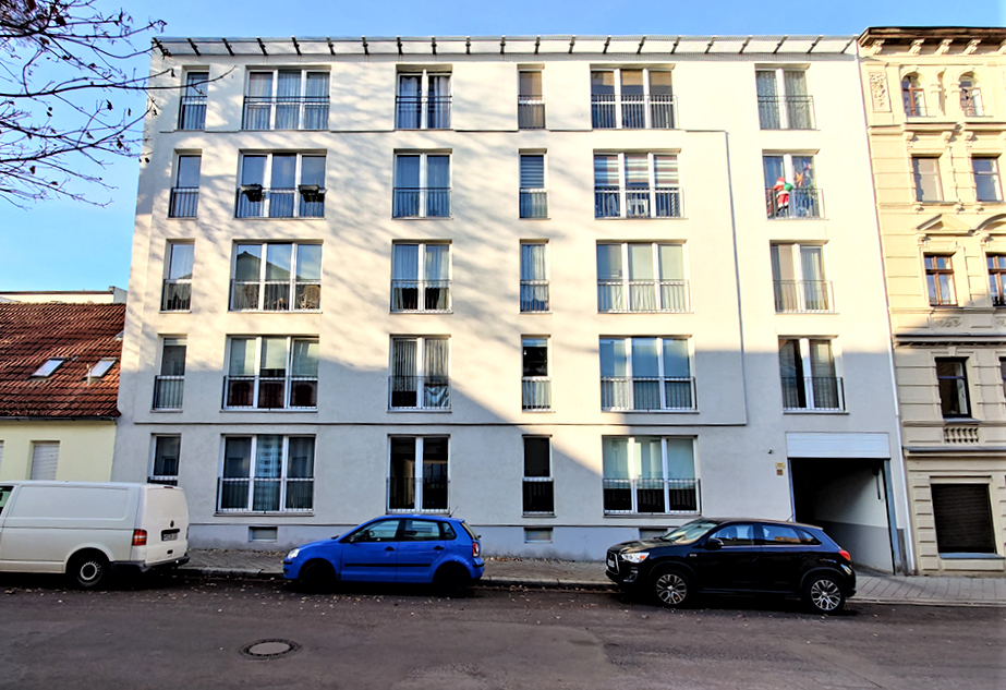 Moderne Stra&szlig;enansicht eines Mehrfamilienhauses mit gro&szlig;en Fenstern und geparkten Autos, zentrales urbanes Wohnen.