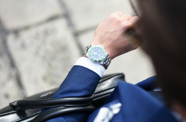 Geschäftsperson im blauen Anzug blickt auf Armbanduhr, Symbol für Zeitmanagement und Business-Alltag.