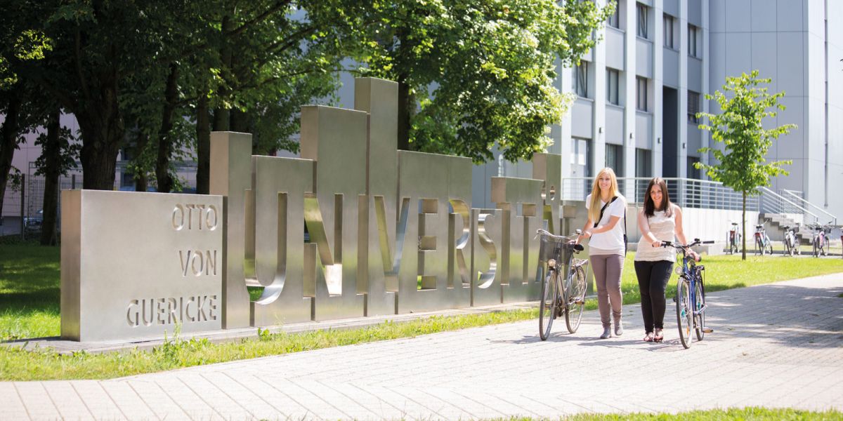 Otto-von-Guericke-Universit&auml;t Magdeburg, Studierende mit Fahrr&auml;dern vor Uniskulptur auf gr&uuml;nem Campus.
