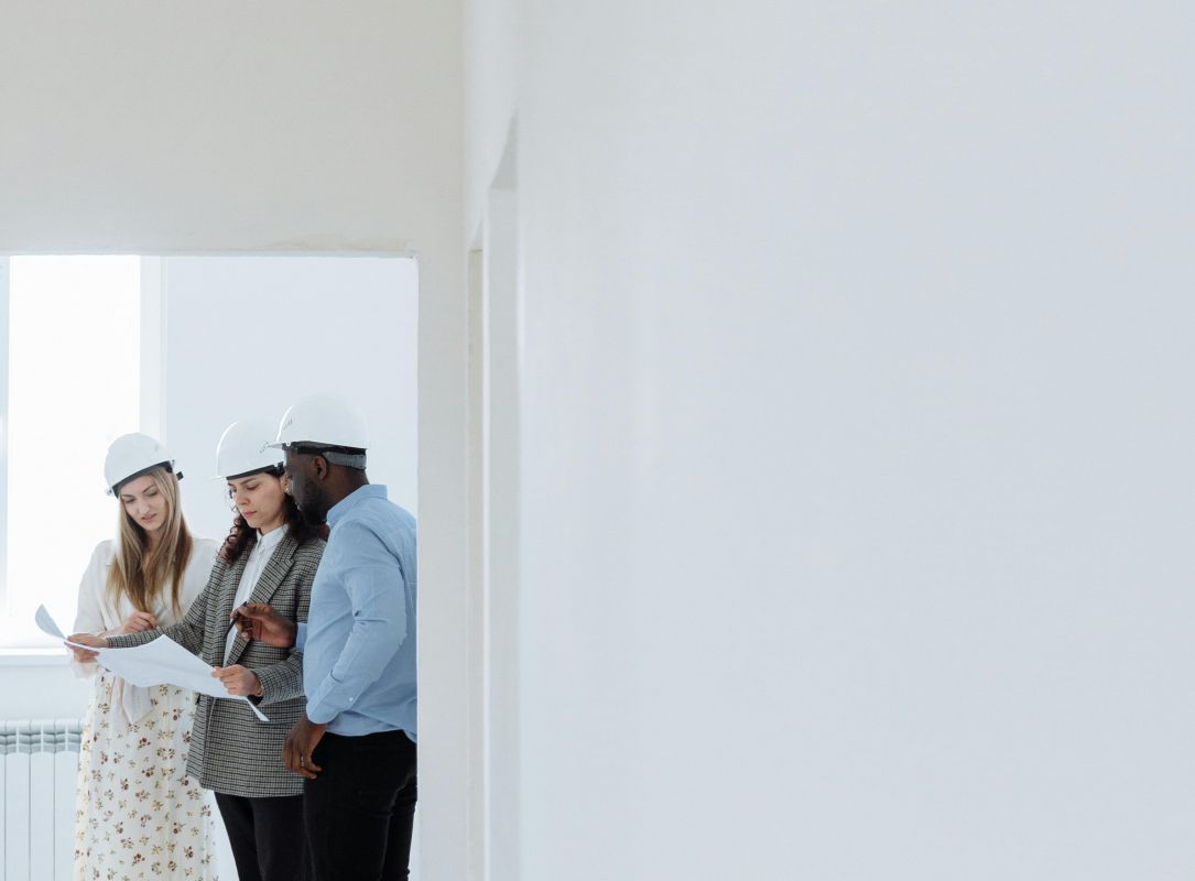 Team mit Bauhelmen prüft Baupläne im Rohbau, Baustellenbesichtigung und Projektbesprechung im Innenraum.