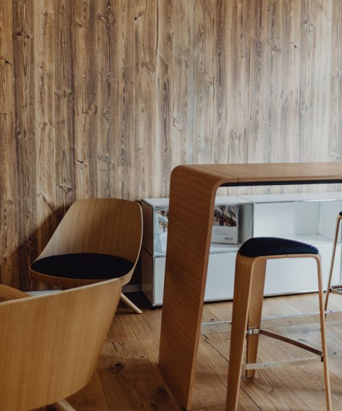 Moderner Besprechungsbereich mit Holztisch, Holzstühlen und Holzwand, minimalistisches und warmes Raumdesign.